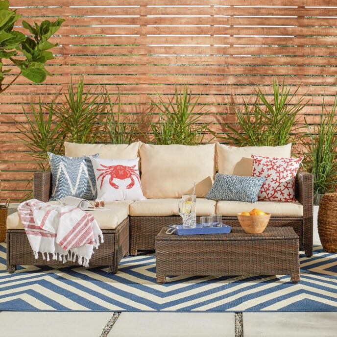 Outdoor patio scene with a brown rattan couch decorated with red, white, & blue throw pillows on a blue chevron rug