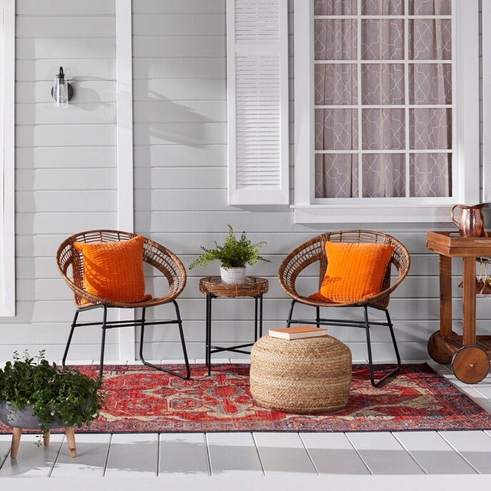 A pair of round wicker chairs on the front porch of a light grey home with orange throw pillows available at Overstock